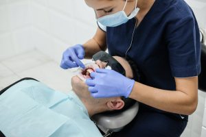 A male patient wears sunglasses to protect his eyes while a hygienist works on his mouth.